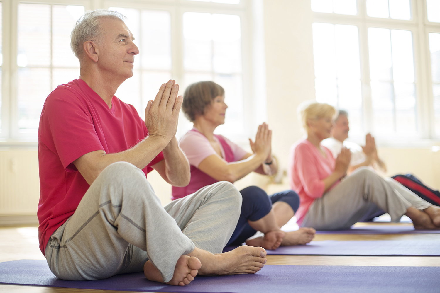 Senior man sitting in lotus position doing meditation with group of people in yoga class
