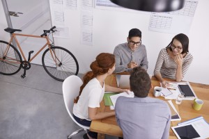 four coworkers sitting at a table talking and working